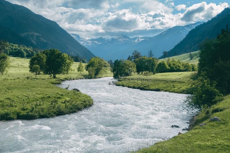 A wide view of the Langtang Valley floor with a river, yak pastures, and snow-capped peaks in the background